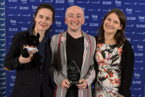 Three members of the Frontrunners, in smart suits and dresses, holding their award